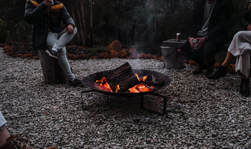 unrecognizable travelers sitting near campfire in woods