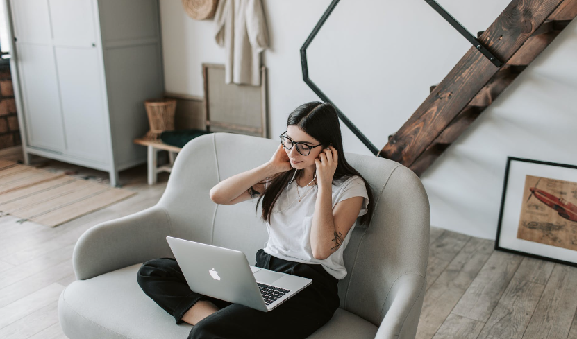 Woman sitting on grey armchair with a laptop in her lap putting headphones in